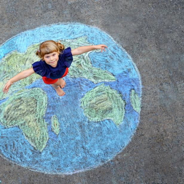 Little preschool girl with earth globe painting with colorful chalks on ground. Positive toddler child. Happy earth day concept. Creation of children for saving world, environment and ecology.