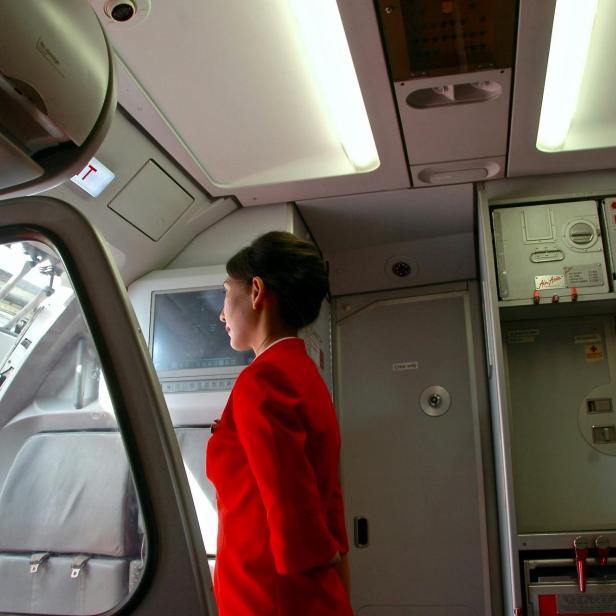 Eine Flugbegleiterin in roter Uniform steht in der geöffneten Flugzeugkabine und blickt zur Tür hinaus.