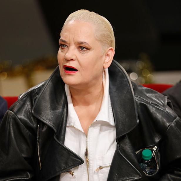 Hella von Sinnen blickt in schwarzer Lederjacke und weißer Bluse zur Seite.