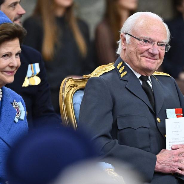 König Carl XVI. Gustaf von Schweden und Königin Silvia sitzen bei einer offiziellen Veranstaltung in festlicher Kleidung nebeneinander.