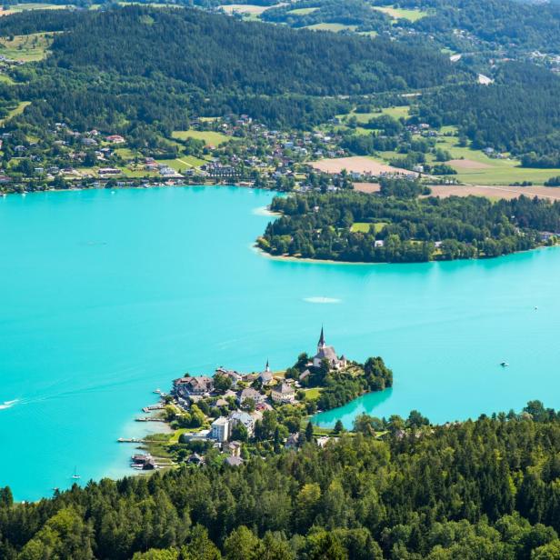 Blick auf den türkisblauen Wörthersee mit einer kleinen Halbinsel und Kirche.