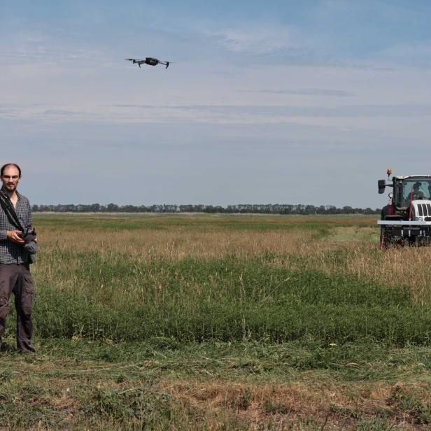 Mann steuert eine Drohne über einem Feld, neben einem Traktor.