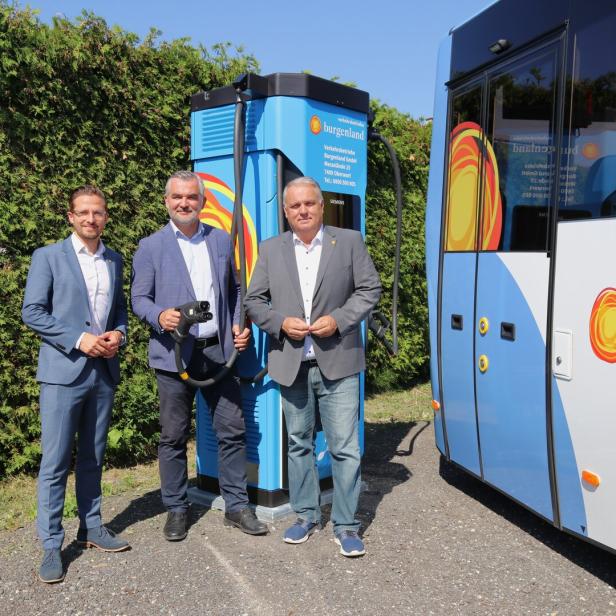 Drei Männer stehen neben einem Linienbus und einer blauen Ladesäule für Elektrofahrzeuge.