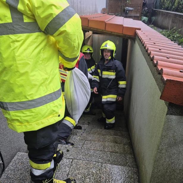 Feuerwehrleute tragen Sandsäcke durch einen engen Kellerabgang.