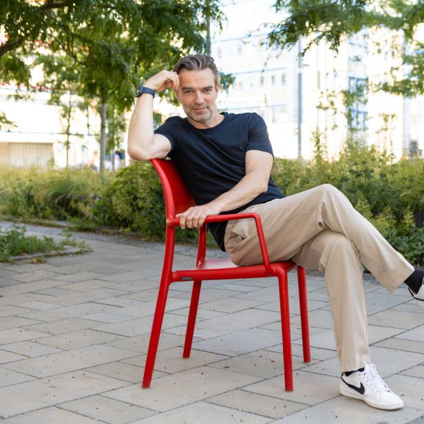 Jakob Seeböck sitzt entspannt auf einem roten Stuhl im Park.
