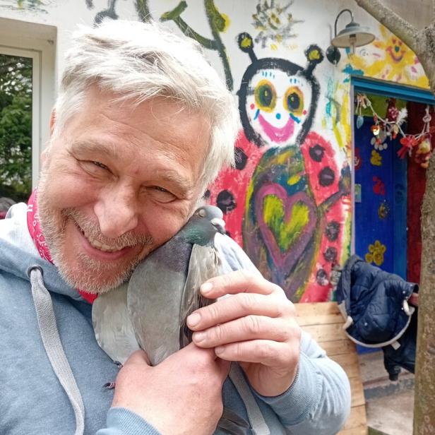 Lächelnder Mann hält eine Taube vor einer bunt bemalten Wand.