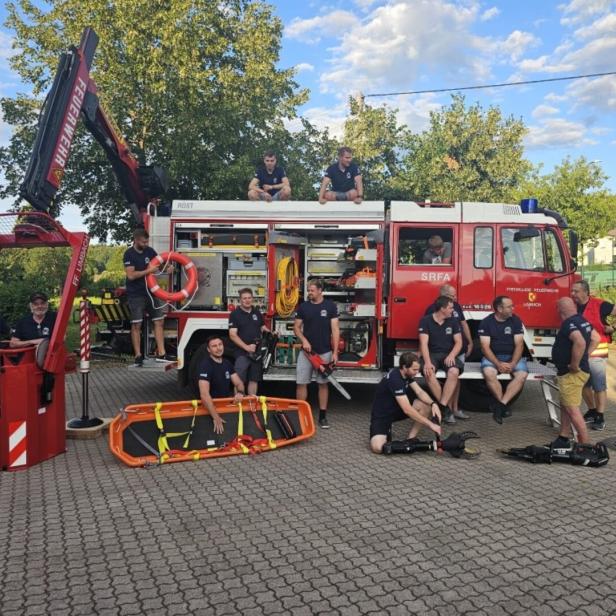 Mehrere Feuerwehrleute stehen und sitzen an einem roten Einsatzfahrzeug mit Rettungsgerät und geöffneter Geräteraumklappe.