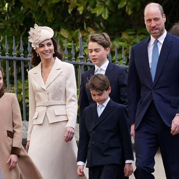 Prinz William und Prinzessin Catherine gehen mit ihren Kindern George, Charlotte und Louis vor einem Zaun spazieren.
