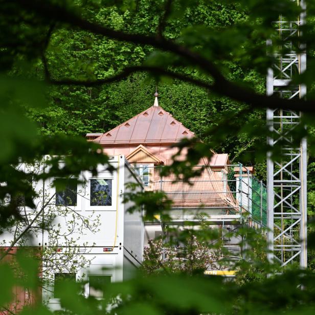 Baustelle mit Kupferdach zwischen dichtem Wald, im Vordergrund verdeckte Container und ein Metallgerüst.