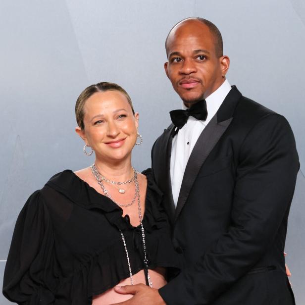Jennifer Meyer in einem schwarzen Oberteil und Geoff Ogunlesi im Smoking stehen eng beieinander vor einem hellgrauen Hintergrund.