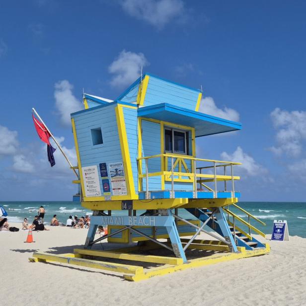 Bunte Rettungsschwimmerhütte am Strand von Miami Beach mit Sonne, Meer und Badenden.