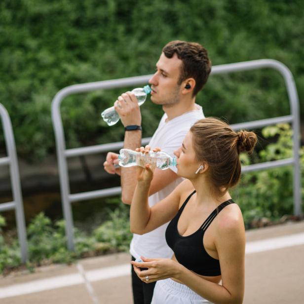 Zwei junge Menschen trinken während des Sports Wasser im Freien.