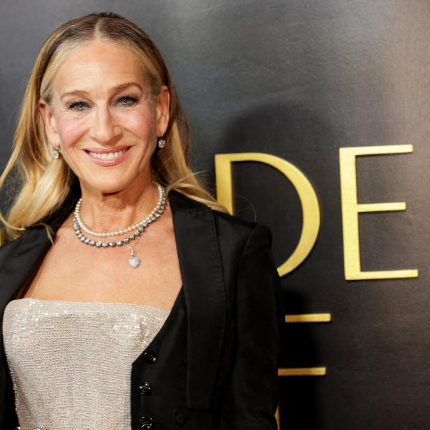 Sarah Jessica Parker lächelt vor einem schwarzen Hintergrund mit goldenem Schriftzug.