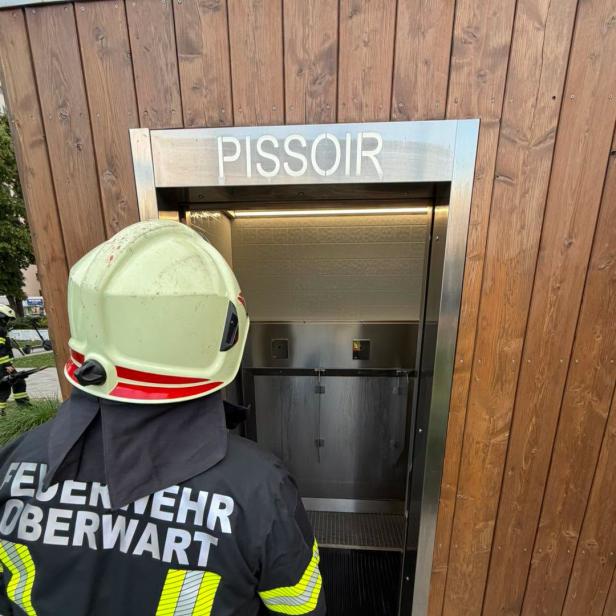Feuerwehrmann vor öffentlicher Toilettenanlage mit offener Tür.