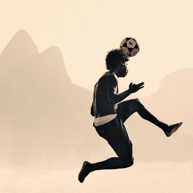 Ein junger Mann jongliert vor der Silhouette des Zuckerhuts in Rio de Janeiro einen Fußball mit dem Kopf.