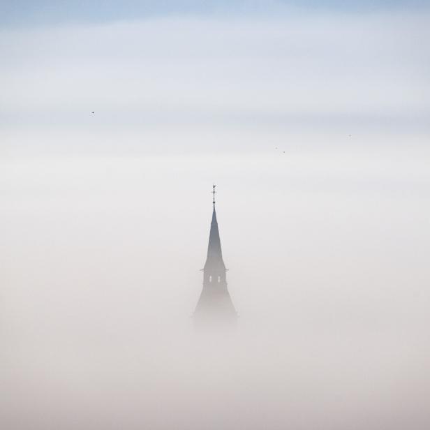 Kirchturmspitze ragt aus dichtem Nebel empor.