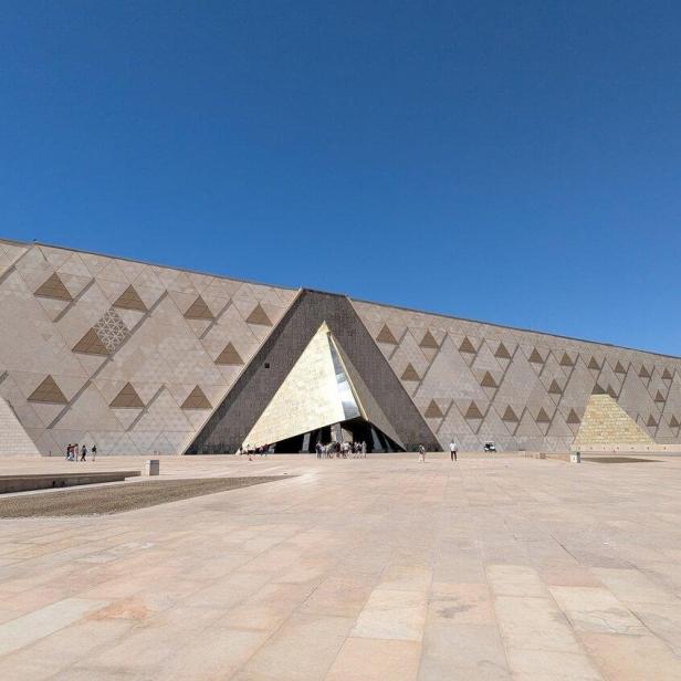 Die Fassade des Grand Egyptian Museum in Gizeh mit ihrem markanten dreieckigen Eingang vor einem klaren blauen Himmel.