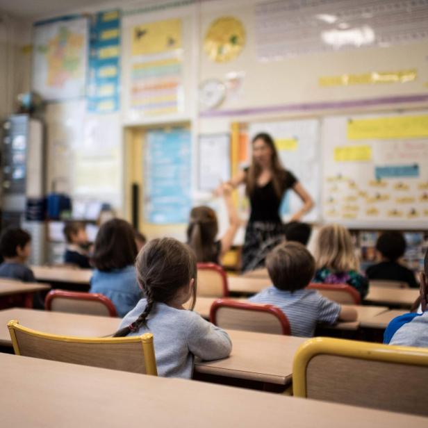 Lehrerin erklärt vor einer Grundschulklasse den Stoff, während die Kinder an Tischen sitzen und zuhören.
