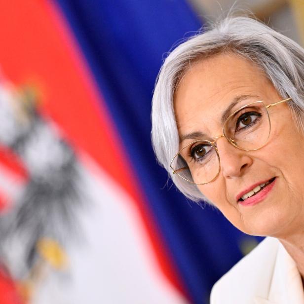 Ältere Frau mit Kurzhaarschnitt und Brille vor unscharfem rot-blauem Hintergrund.