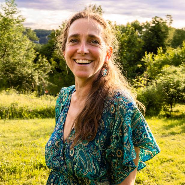 Lächelnde Frau im grünen Feld vor Bäumen und Himmel.