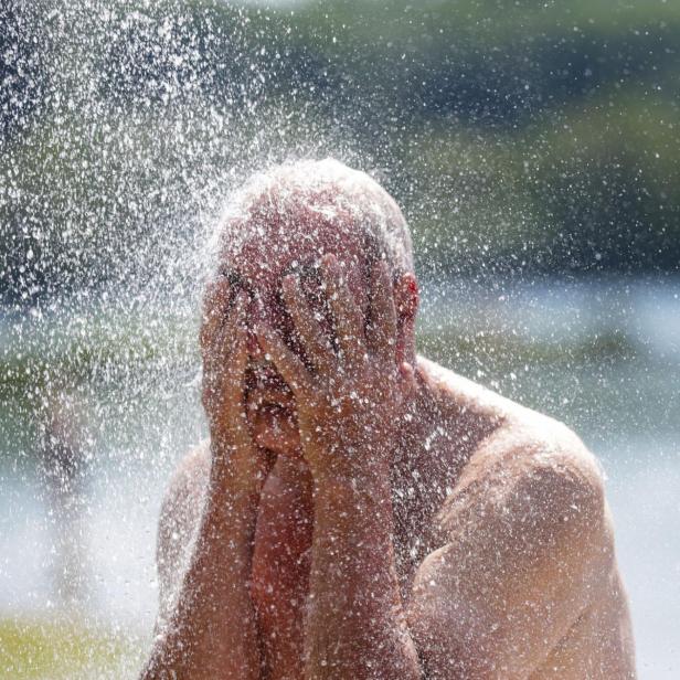 Ein Mann kühlt sich mit Wasserstrahlen ab und bedeckt im Hitzestress sein Gesicht.