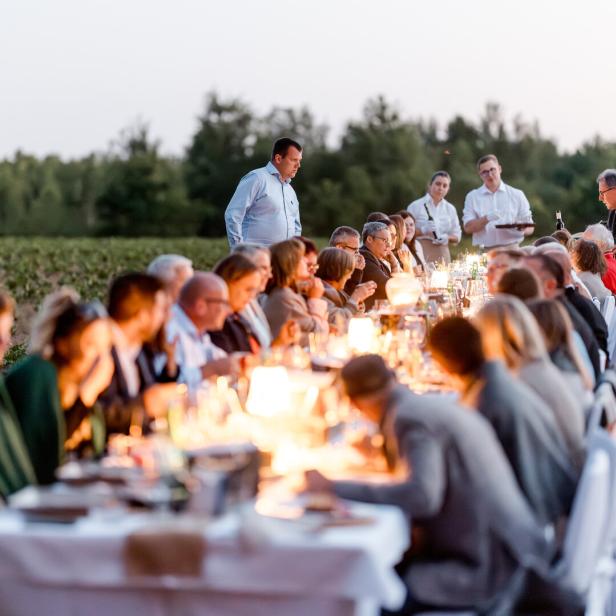 Lange Tafel mit Gästen und Kerzenlicht im Freien zwischen Feldern bei einer Abendveranstaltung der Waldviertler Tischkultur 2025.