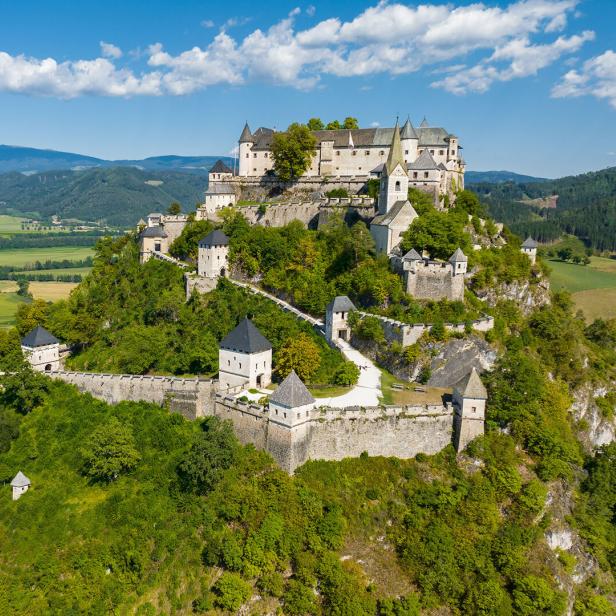 Die Burg Hochosterwitz thront auf einem bewaldeten Felskegel inmitten einer grünen Hügellandschaft in Kärnten.