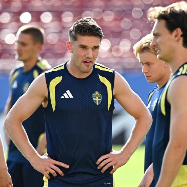 Spieler der schwedischen Fußballnationalmannschaft in dunkelblauen Trainingsshirts mit gelben Akzenten stehen auf einem Sportplatz.