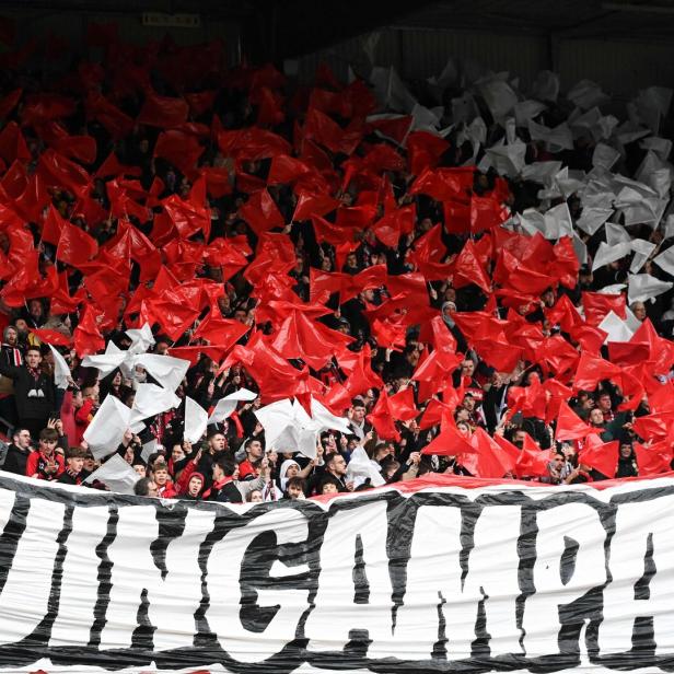 Fans von En Avant Guingamp schwenken im Stadion zahlreiche rote und weiße Fahnen hinter einem großen Banner mit der Aufschrift „GUINGAMPAIS“.