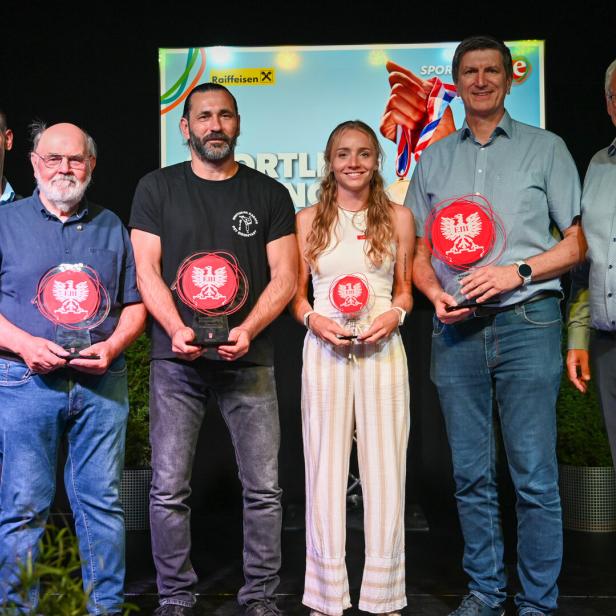 Sechs Personen stehen auf einer Bühne und halten Sporttrophäen vor einem Event-Hintergrund.