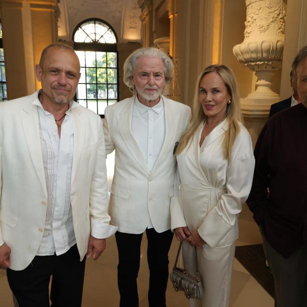 Vier elegant gekleidete Personen stehen in einer prunkvollen Halle und schauen in die Kamera.