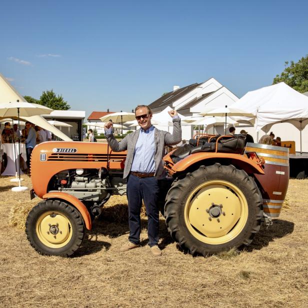 Mann posiert lächelnd neben einem orangefarbenen Diesel-Traktor auf einer Feier im Freien.