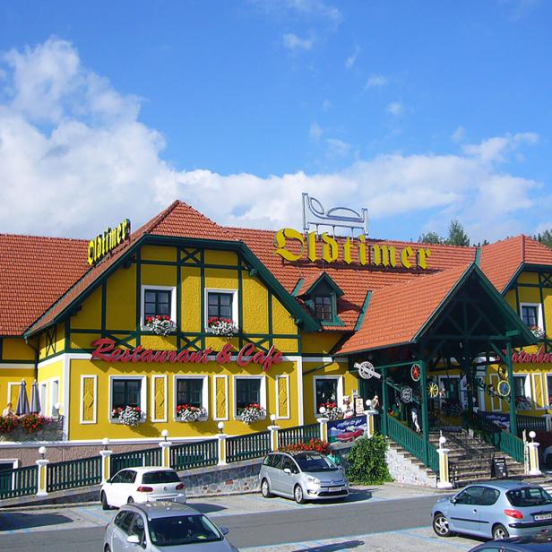 Das gelbe Oldtimer Restaurant & Café mit rotem Ziegeldach und Parkplatz davor unter blauem Himmel.