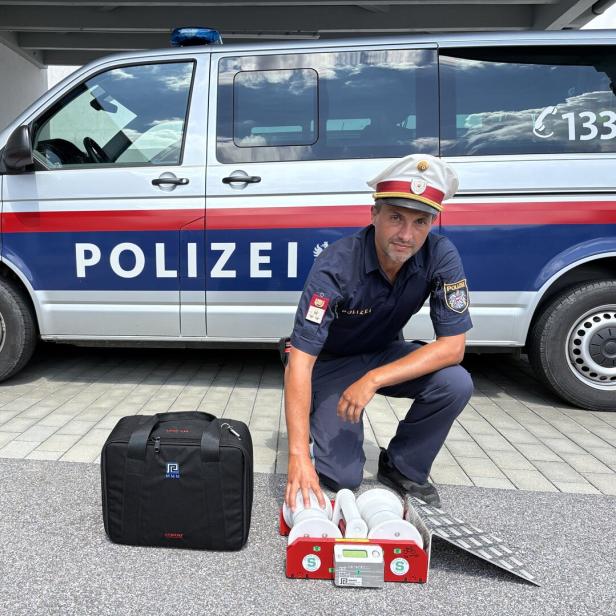 Polizist kniet vor einem Polizeiwagen neben Einsatzgerät und Tasche.
