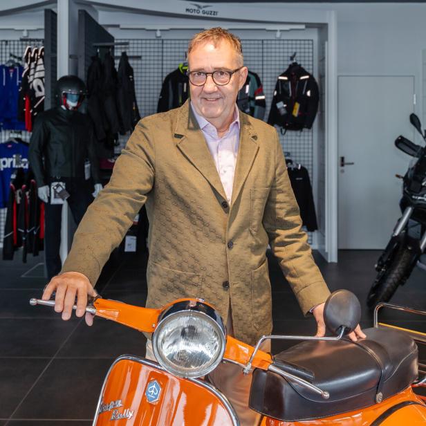Josef Faber steht in einem Motorradladen hinter einer orangefarbenen Vespa.