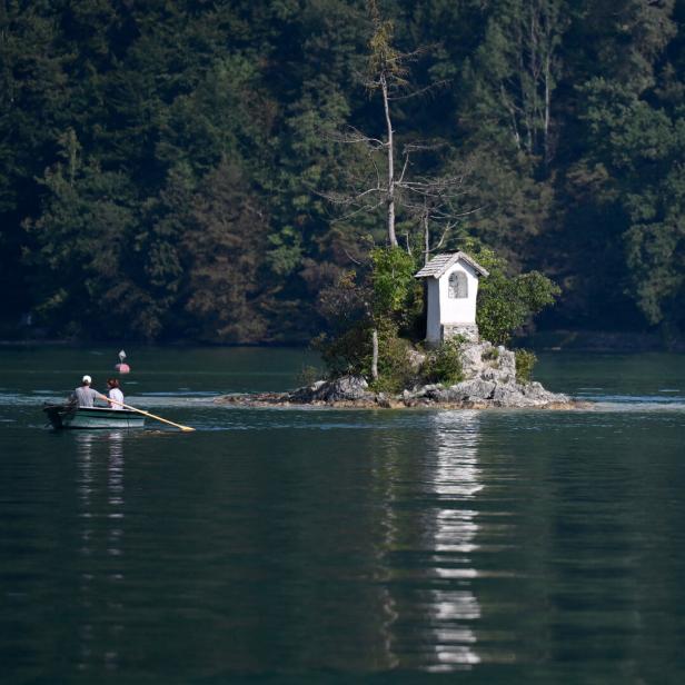 Ein Boot mit zwei Personen auf einem See neben einer kleinen Insel mit Kapelle.