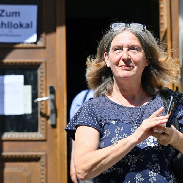 Eine Frau mit Brille auf dem Kopf verlässt ein Gebäude, an dessen Tür ein Schild mit der Aufschrift „Zum Wahllokal“ hängt.
