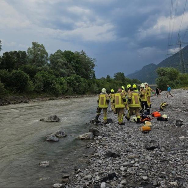 Feuerwehrleute in Schutzkleidung stehen am Ufer eines Flusses unter dunklen Wolken und bereiten Ausrüstung vor.