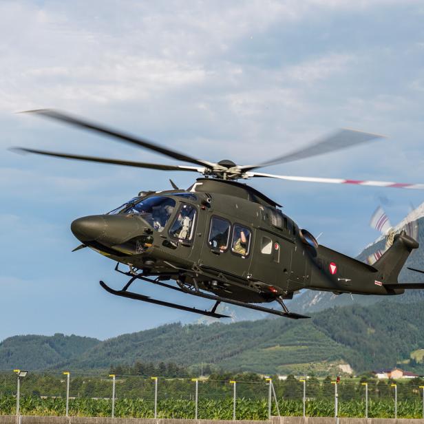 Ein olivgrüner Hubschrauber des Österreichischen Bundesheeres fliegt vor einer Bergkulisse.