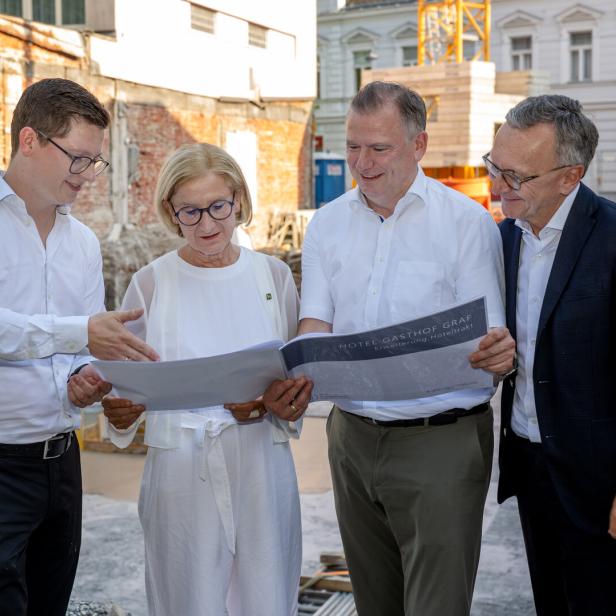 Vier Personen betrachten gemeinsam Pläne auf einer Baustelle.