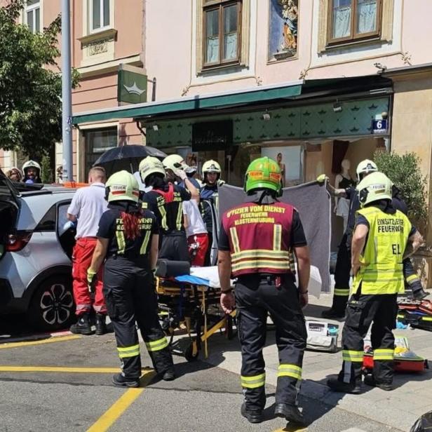Feuerwehrleute versorgen eine Person neben einem geöffneten Auto bei einem Einsatz auf der Straße.