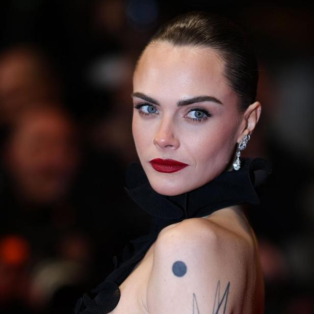 Cara Delevingne blickt mit rotem Lippenstift und hochgesteckten Haaren in die Kamera.