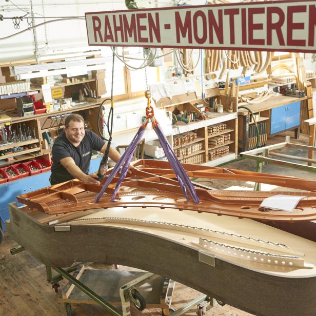 Ein Handwerker montiert in einer Werkstatt einen Flügelrahmen unter einem Schild „RAHMEN-MONTIEREN“.