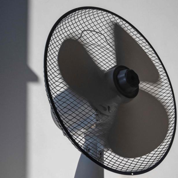 Ein schwarzer Ventilator mit Schutzgitter wirft Schatten an die Wand.