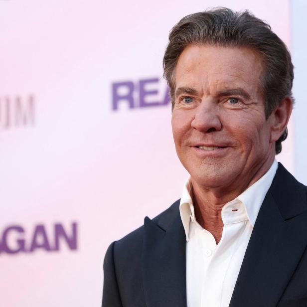 Dennis Quaid lächelt vor einem Hintergrund mit dem Schriftzug „Reagan“ in die Kamera.