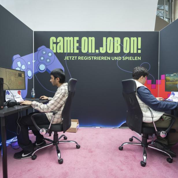 Zwei junge Männer spielen an PCs auf einer Gaming-Messe mit großem „Game on. Job on!“-Banner.