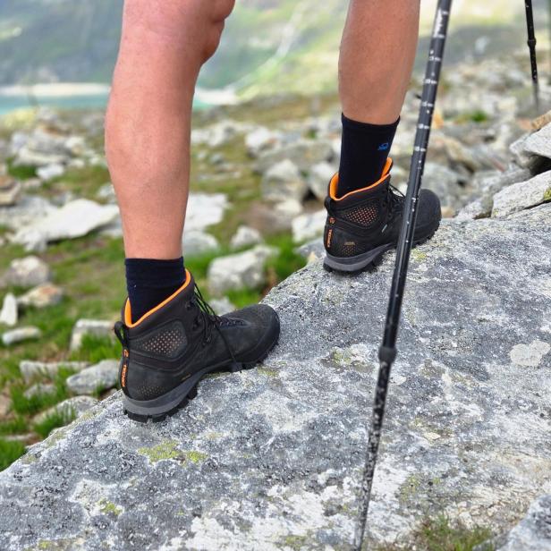 Wanderer mit Trekkingstöcken steht auf einem Felsen in den Bergen.