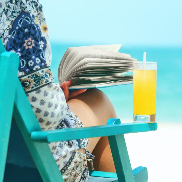 Woman sitting in deck chair at beach reading book on sunny day.