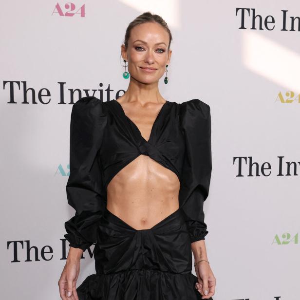 Olivia Wilde trägt ein schwarzes Kleid mit Cut-out vor einer A24-Hintergrundwand.