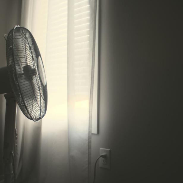 Weißer Standventilator steht in einem abgedunkelten Raum am Fenster
